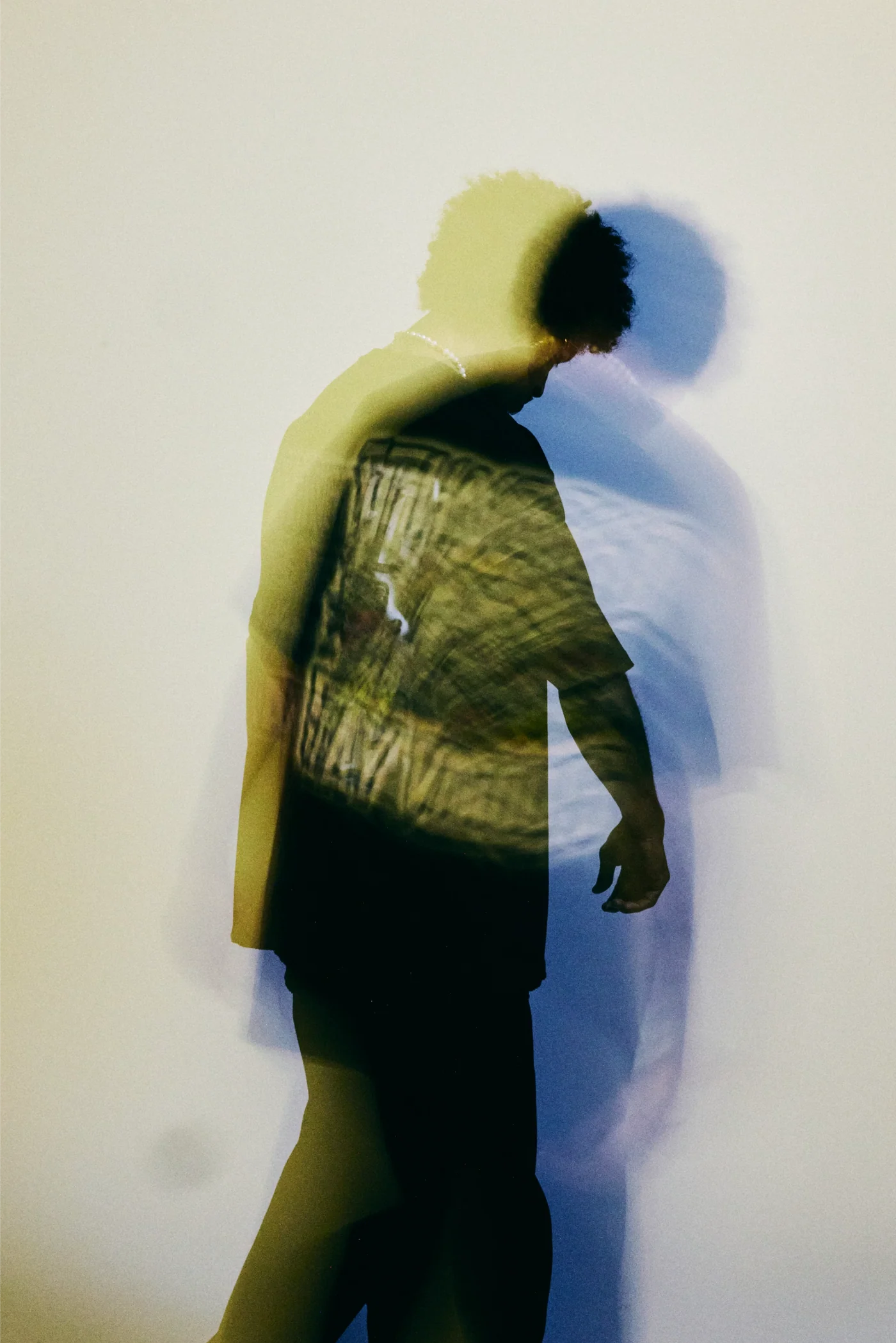 Blurred double-exposure portrait of a person in a printed T-shirt, lit in yellow and blue